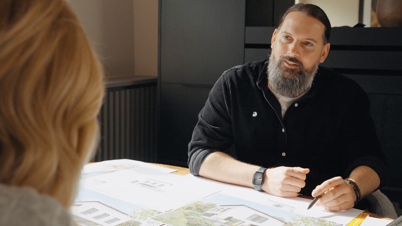Thumbnail eines Expertenvideos von FingerHaus, ein Architekt im Gespräch mit einer Person an einem Tisch mit Bauplänen.