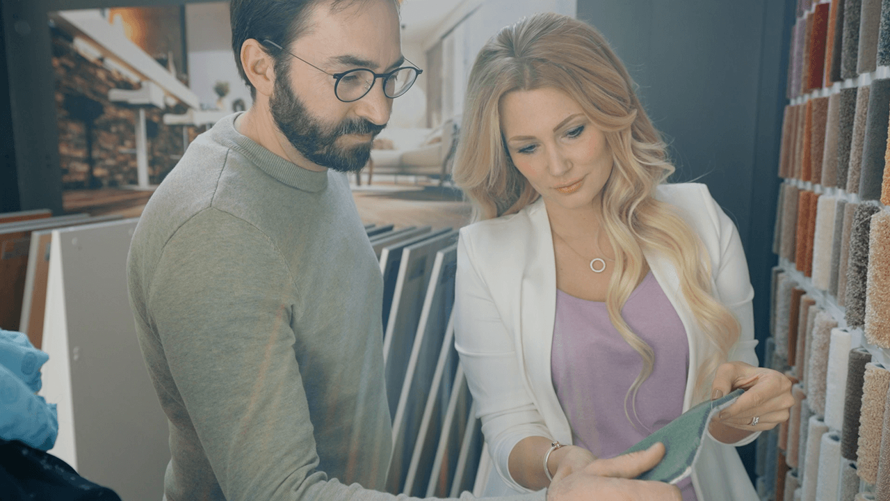 Thumbnail eines Expertenvideos von FingerHaus, eine Ausstattungsberaterin im Gespräch mit einer Person in einem Showroom mit Musterflächen und Materialien.