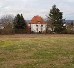 Freies Baugrundstück in Bad Wildungen mit Blick auf eine Villa und Bäume im Hintergrund.
