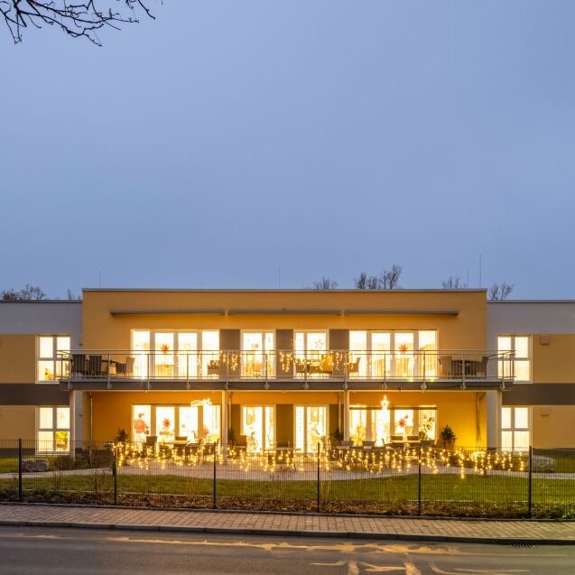 Zweigeschossiger Pflegeheim-Neubau in Adorf in der Abenddämmerung. Das moderne Gebäude von FingerHaus ist vollständig beleuchtet und zeigt eine klare, symmetrische Architektur mit Balkonen und großzügigen Fensterfronten.