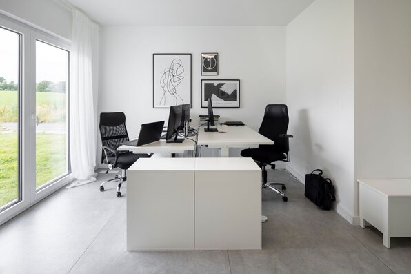 Modernes Homeoffice mit zwei Schreibtischen, ergonomischen Stühlen und großem Fenster mit Blick ins Grüne in einem frei geplanten FingerHaus.