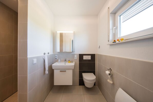 Modernes Gäste-WC in einem frei geplanten FingerHaus mit Wand-WC, Waschbecken und großformatigen Fliesen.