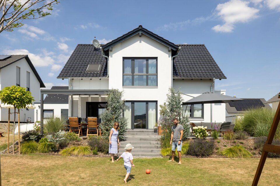 Familie mit Kind spielt auf dem Rasen vor einem Einfamilienhaus SENTO 403 mit Satteldach, Terrasse und angelegtem Garten