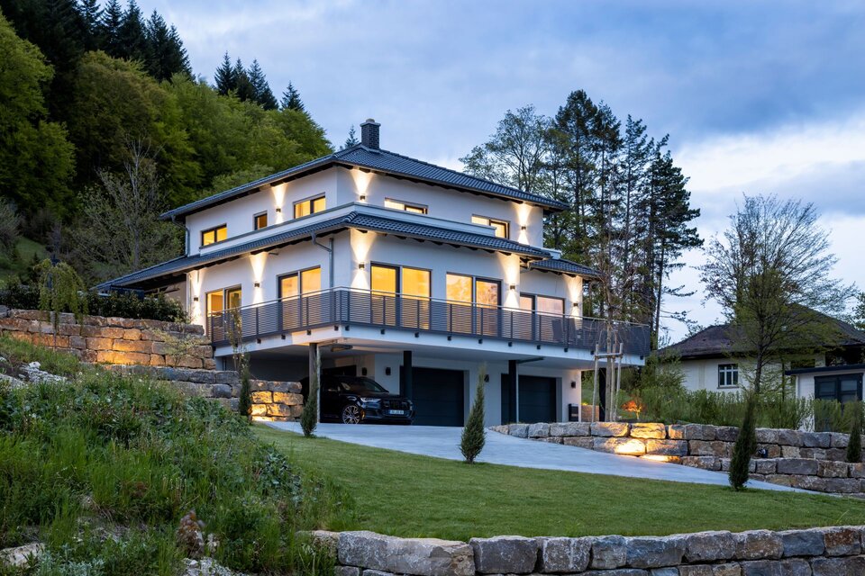 Modernes FingerHaus mit Walmdach und umlaufendem Balkon, stimmungsvoll beleuchtet in der Abenddämmerung.