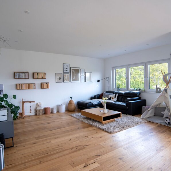 Großzügiges Wohnzimmer in einem frei geplanten FingerHaus mit heller Einrichtung, Holzboden, schwarzem Sofa und moderner Deko.