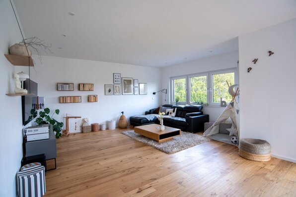 Großzügiges Wohnzimmer in einem frei geplanten FingerHaus mit heller Einrichtung, Holzboden, schwarzem Sofa und moderner Deko.