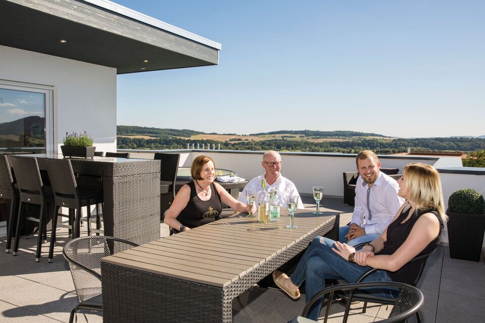 Vier Personen sitzen entspannt auf der Dachterrasse eines modernen FingerHaus und genießen gemeinsam das schöne Wetter und die Aussicht.