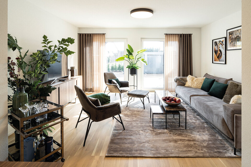 Wohnzimmer mit großer Sitzlandschaft, Sesseln und TV-Bereich; heller Raum mit Teppich und Pflanzen.