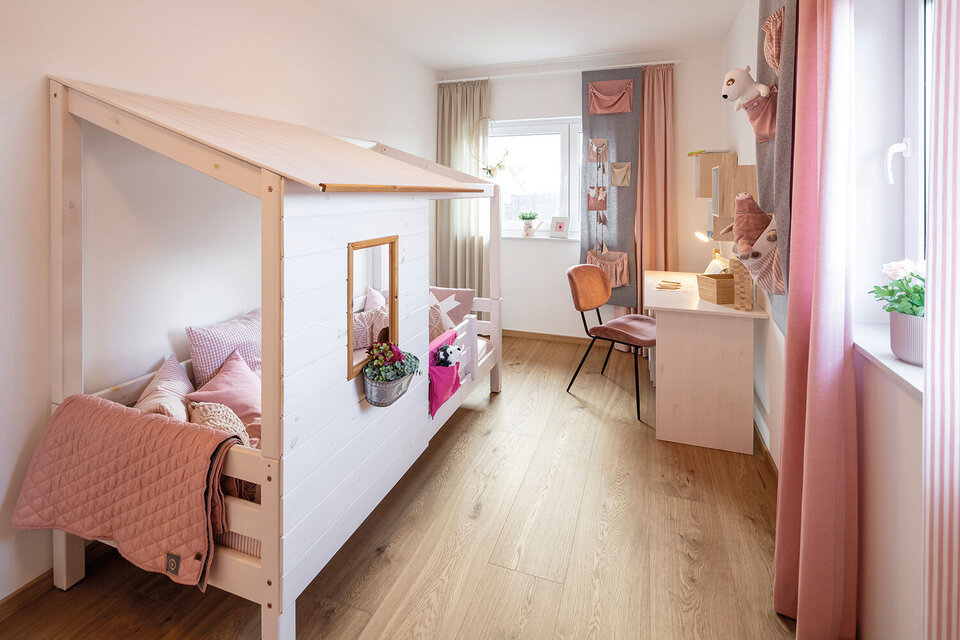 Kinderzimmer mit Hausbett aus Holz, rosa Textilien, Schreibtisch am Fenster und dekorativen Accessoires.