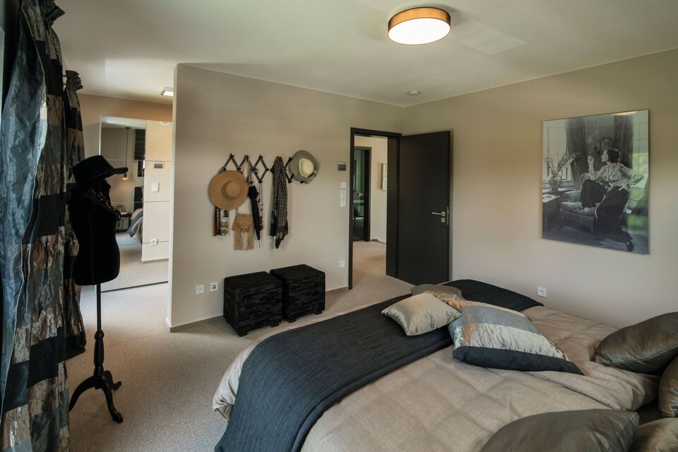 Gemütliches Schlafzimmer im Musterhaus ALTERO in Gießen mit Doppelbett, eleganter Wanddekoration und praktischer Garderobe.