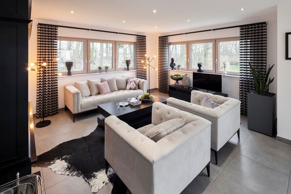 Helles Wohnzimmer im Musterhaus NEO 312 in Bad Vilbel mit großen Fenstern, modernen Sofas und stilvoller Einrichtung.