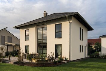 Zweigeschossiges Einfamilienhaus mit Walmdach, großer Fensterfront und gepflegtem Garten auf einem Grundstück in einem Wohngebiet.