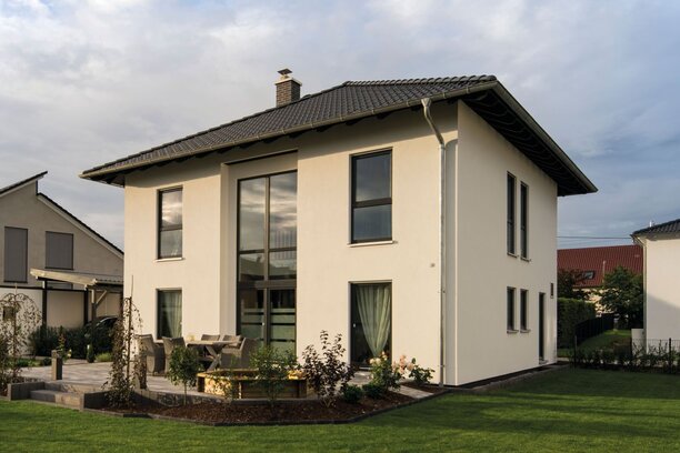 Zweigeschossiges Einfamilienhaus mit Walmdach, großer Fensterfront und gepflegtem Garten auf einem Grundstück in einem Wohngebiet.