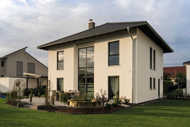 Zweigeschossiges Einfamilienhaus mit Walmdach, großer Fensterfront und gepflegtem Garten auf einem Grundstück in einem Wohngebiet.