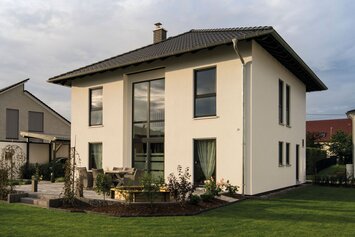 Zweigeschossiges Einfamilienhaus mit Walmdach, großer Fensterfront und gepflegtem Garten auf einem Grundstück in einem Wohngebiet.