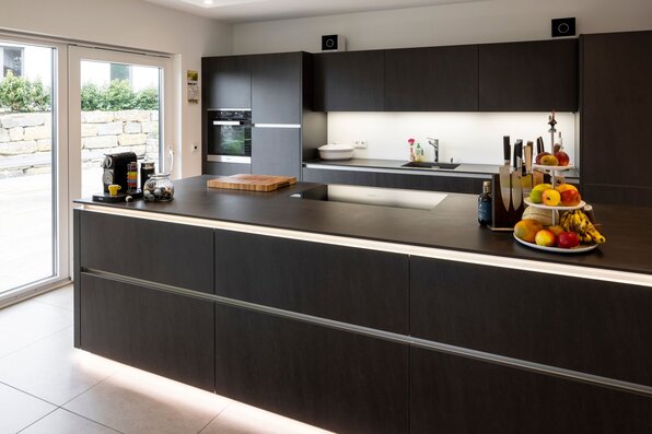 Moderne FingerHaus-Küche mit dunklen Fronten, großer Kochinsel, Induktionskochfeld und dekorativer Obstschale.