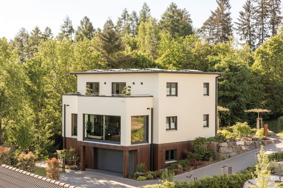Modernes, frei geplantes FingerHaus mit klaren Linien, großzügigen Fensterflächen und integrierter Garage, eingebettet in grüne Umgebung.