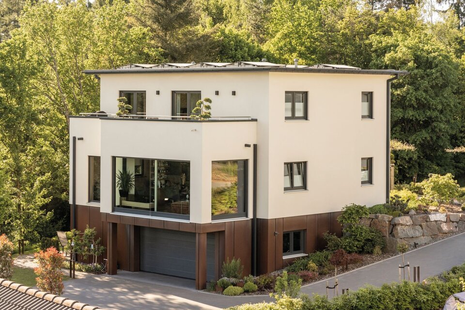 Modernes, frei geplantes FingerHaus mit klaren Linien, großzügigen Fensterflächen und integrierter Garage, eingebettet in grüne Umgebung.
