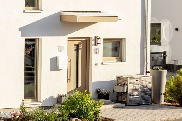 Zweigeschossiges weißes Einfamilienhaus mit dunklem Satteldach, angebauter Garage und gepflastertem Vorplatz.