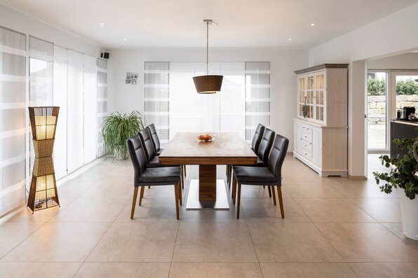 Heller Essbereich in einem FingerHaus mit großem Holztisch, sechs Lederstühlen, Vitrinenschrank und dekorativer Stehlampe.