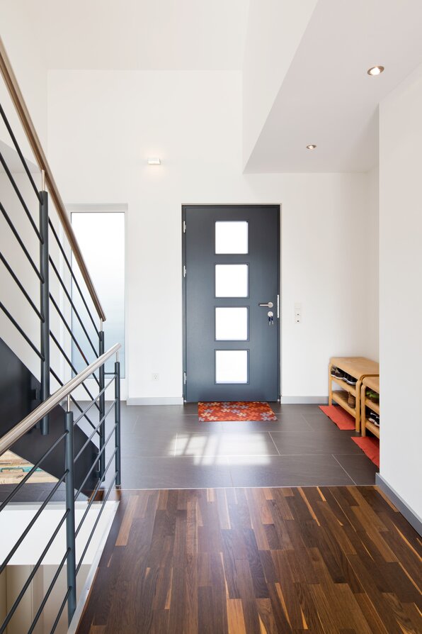 Moderner Eingangsbereich mit dunkler Haustür, heller Wandgestaltung und stilvollem Kontrast aus Fliesen- und Holzboden.
