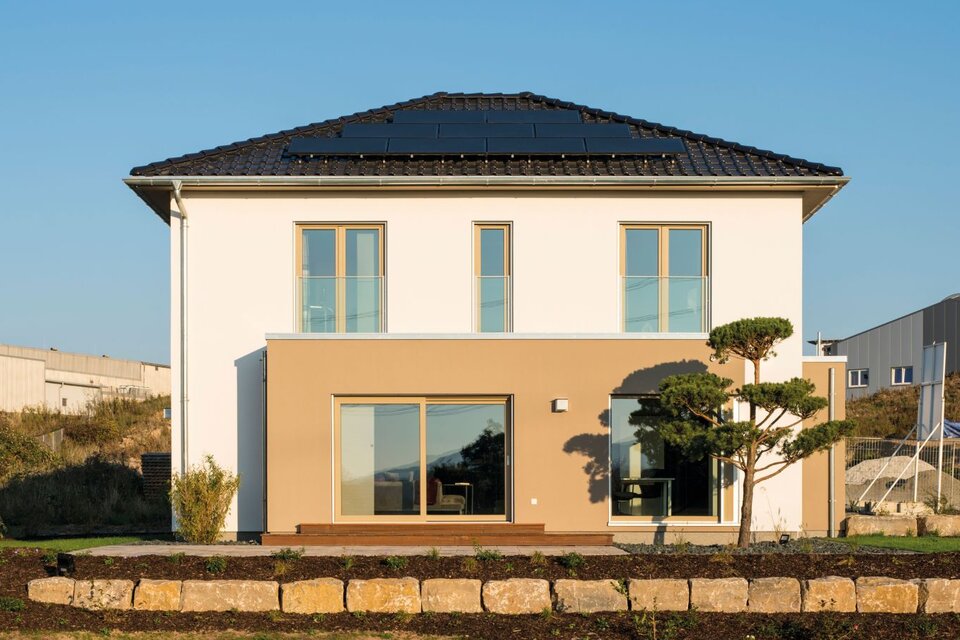 Rückansicht des Musterhauses MEDLEY 300 B in Kassel mit großer Fensterfront, Walmdach und modernem Fassadendesign.