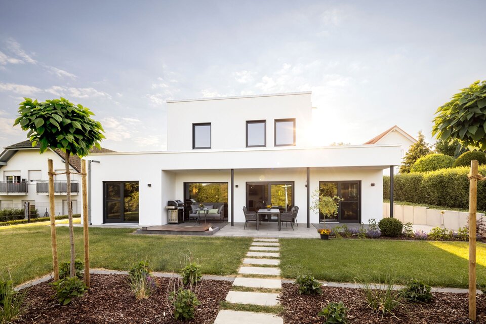 Moderne Außenansicht eines frei geplanten FingerHaus Einfamilienhauses mit weiß verputzter Fassade im kubischen Bauhaus-Stil. Mit überdachter Terrasse, großen Fenstern und gepflegtem Garten.