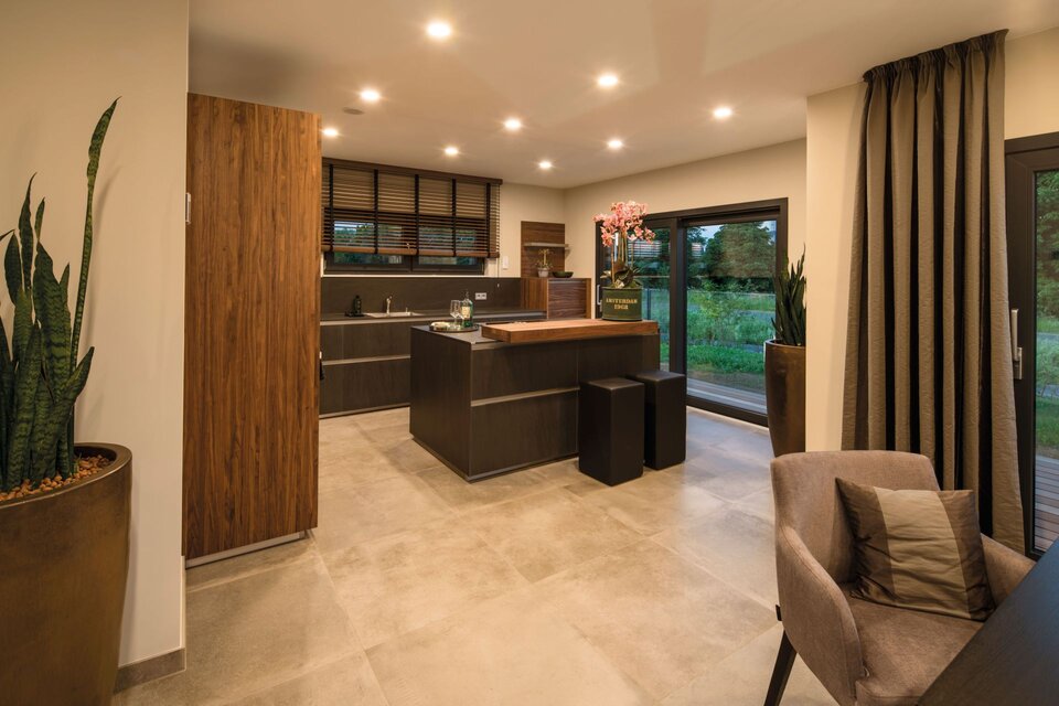 Moderne offene Küche mit Kochinsel, Holzfronten, schwarzen Hockern und großen Fenstern mit Blick ins Grüne