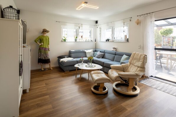 Wohnzimmer eines modernen Bungalows mit Ecksofa, Relaxsessel, Holzboden und Zugang zur Terrasse