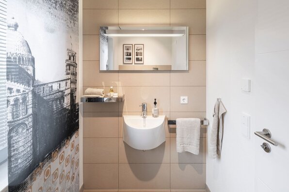 Kompaktes Gäste-WC im frei geplanten FingerHaus Musterhaus Marburg mit Waschbecken, Wandspiegel und dekorativer Fliesenwand.