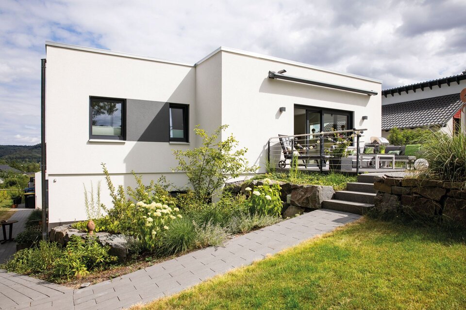 Moderner FingerHaus-Bungalow mit Flachdach, weißer Fassade, Terrasse mit Lounge-Möbeln und gepflegtem Garten mit Treppe.