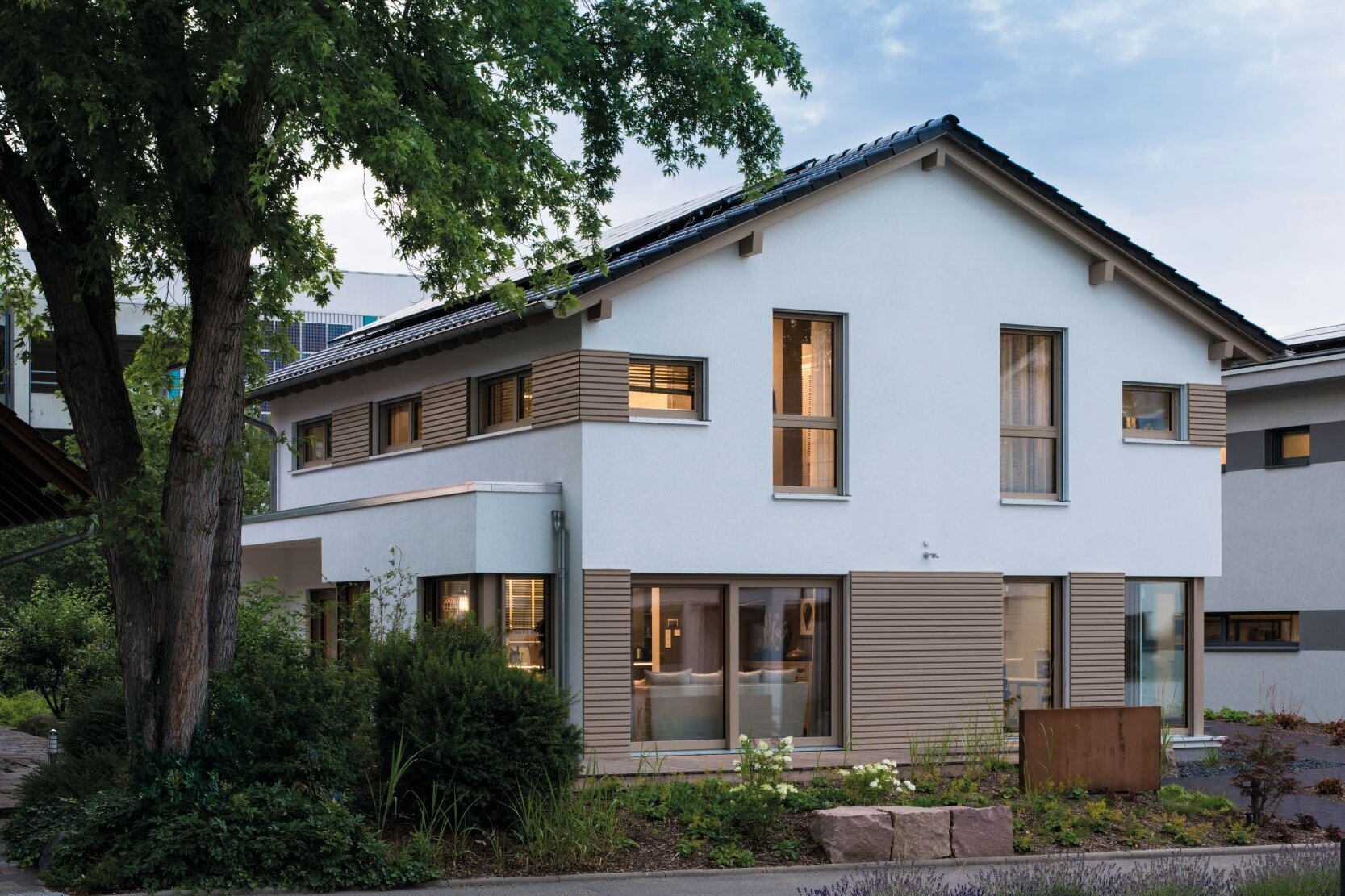 Musterhaus MEDLEY von FingerHaus in Fellbach in der Dämmerung, moderne Putz- und Holzfassade mit großen Fenstern und eingewachsenem Vorgarten.