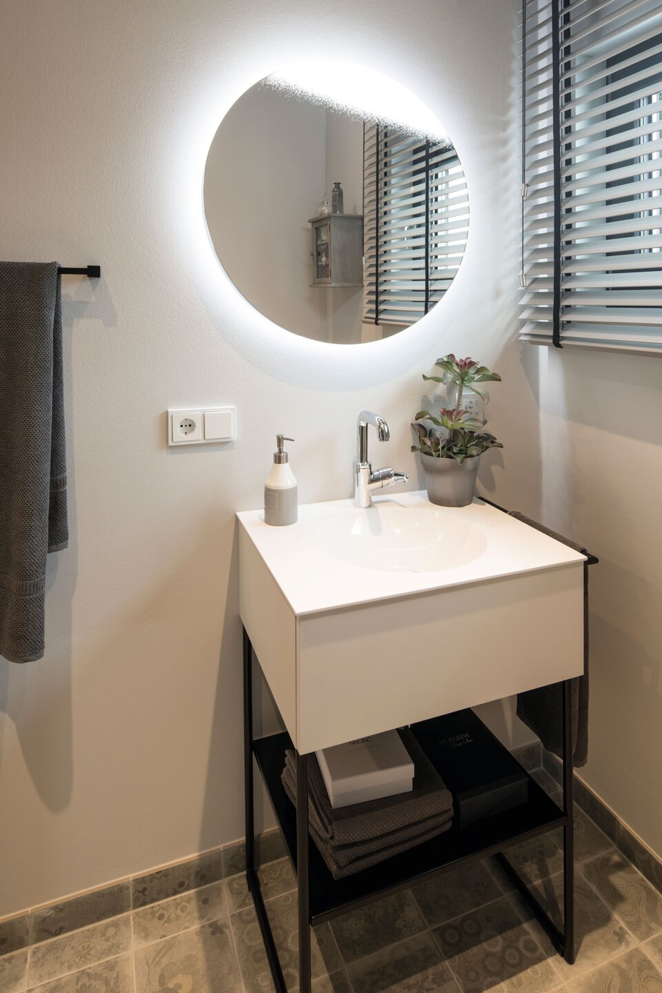 Modernes Gäste-WC im Musterhaus ALTERO in Gießen mit rundem Spiegel und kompaktem Waschtisch.