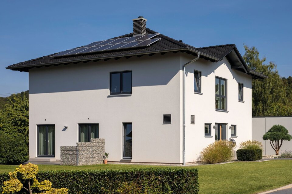 Modernes zweigeschossiges FingerHaus mit weißer Fassade, dunklem Satteldach, Solaranlage auf dem Dach und gepflegtem Vorgarten mit Hecken und Rasenfläche.