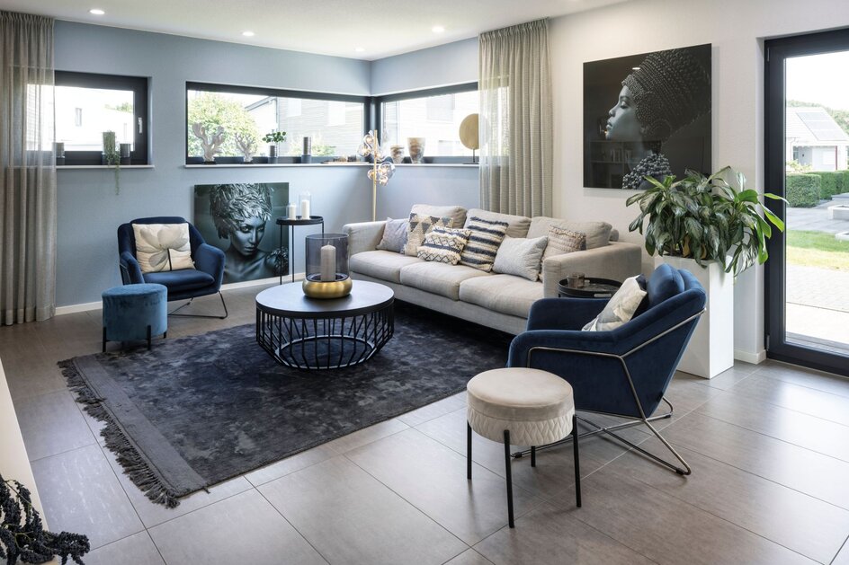 Wohnzimmer im Musterhaus VIO Köln mit grauem Sofa, blauen Sesseln, großformatiger Wandkunst und modernem Interieur.