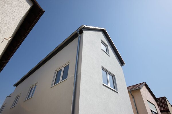 Schlankes, mehrgeschossiges FingerHaus mit Satteldach, klarer Fassade und modernen Fenstern vor blauem Himmel.