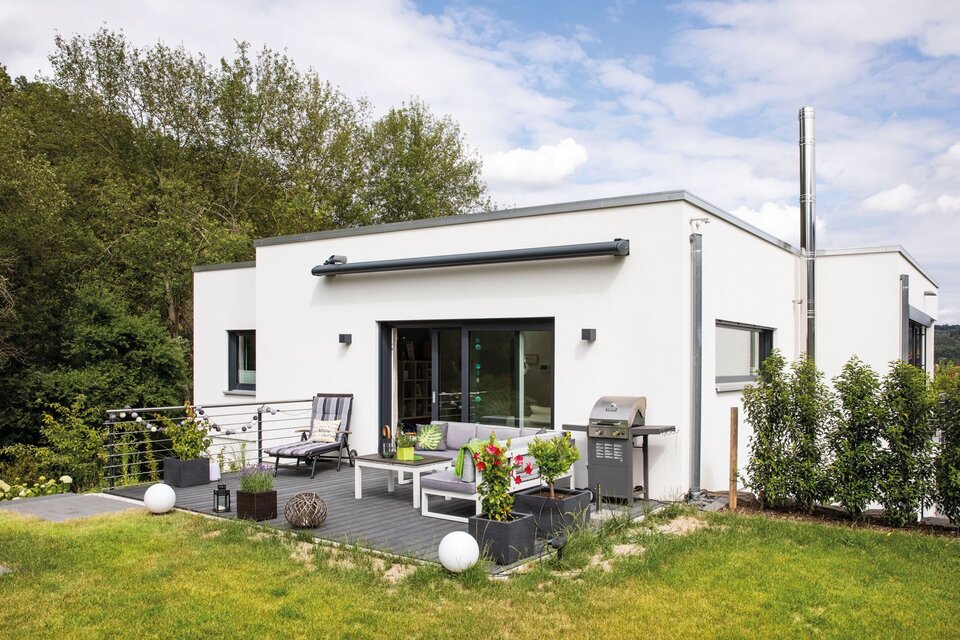 Moderner FingerHaus-Bungalow mit Flachdach, weißer Fassade, großer Terrasse mit Lounge-Möbeln und gepflegtem Garten.