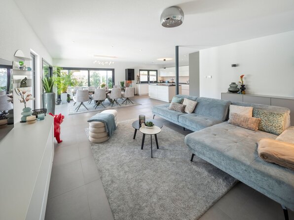 Offener Wohn-, Ess- und Küchenbereich der frei geplanten FingerHaus Stadtvilla mit Ecksofa, Esstisch und moderner Küche.