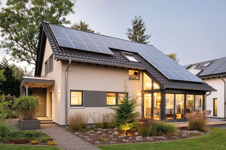Modernes Musterhaus FingerHaus NEO in Wuppertal mit Satteldach, grauer Fassade, Photovoltaikanlage auf dem Dach und einem hell erleuchteten Wintergarten im Erdgeschoss, umgeben von gepflegtem Garten.