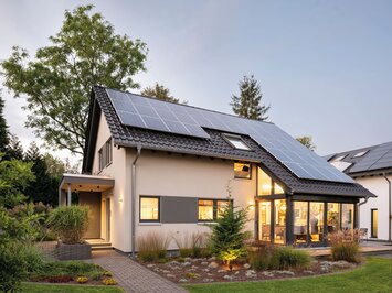 Modernes Musterhaus FingerHaus NEO in Wuppertal mit Satteldach, grauer Fassade, Photovoltaikanlage auf dem Dach und einem hell erleuchteten Wintergarten im Erdgeschoss, umgeben von gepflegtem Garten.