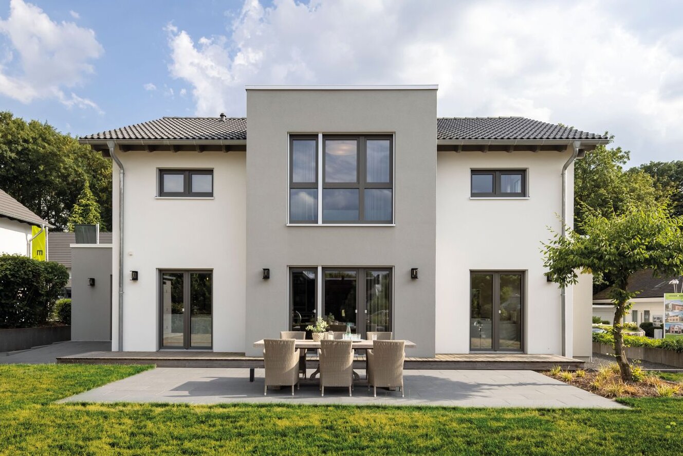 Außenansicht des FingerHaus-Musterhauses SENTO in Bad Vilbel mit moderner, symmetrischer Architektur, heller Putzfassade, großer Terrasse und gepflegtem Garten.
