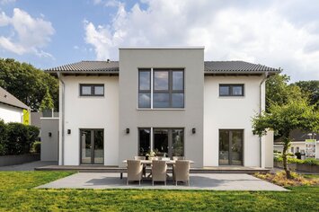 Außenansicht des FingerHaus-Musterhauses SENTO in Bad Vilbel mit moderner, symmetrischer Architektur, heller Putzfassade, großer Terrasse und gepflegtem Garten.