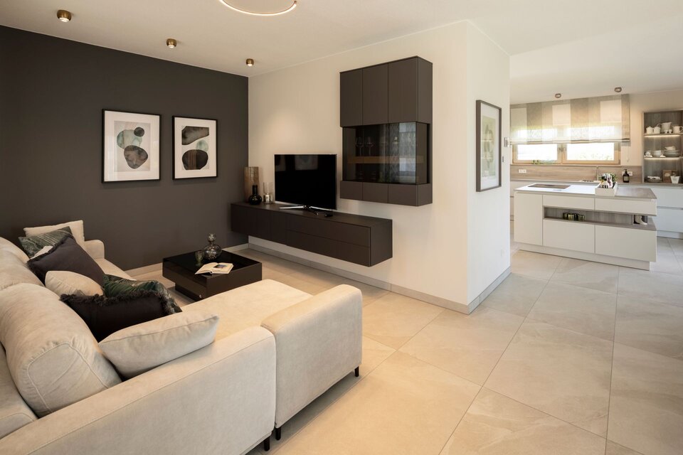 Offener Wohnbereich im FingerHaus ARTIS 300 Musterhaus Nürnberg mit gemütlichem Sofa, modernem TV-Möbel und Blick in die helle Küche mit Kochinsel.