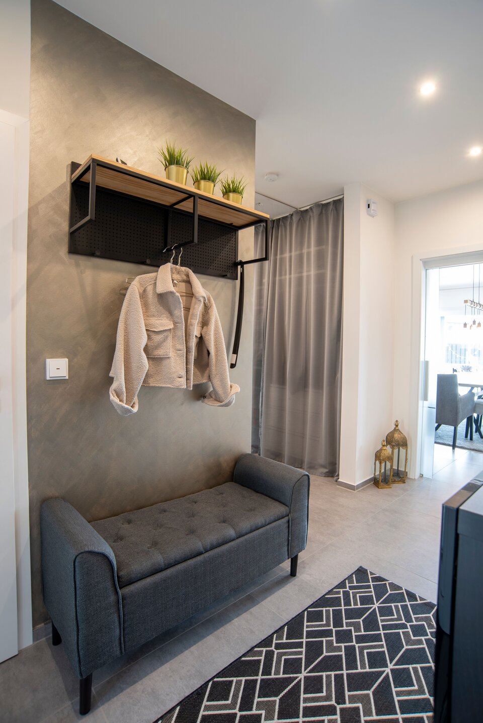 Moderner Eingangsbereich in einem FingerHaus NIVO 130 mit grauer Sitzbank, Garderobe, dekorativen Pflanzen, Wandhaken und Vorhang.