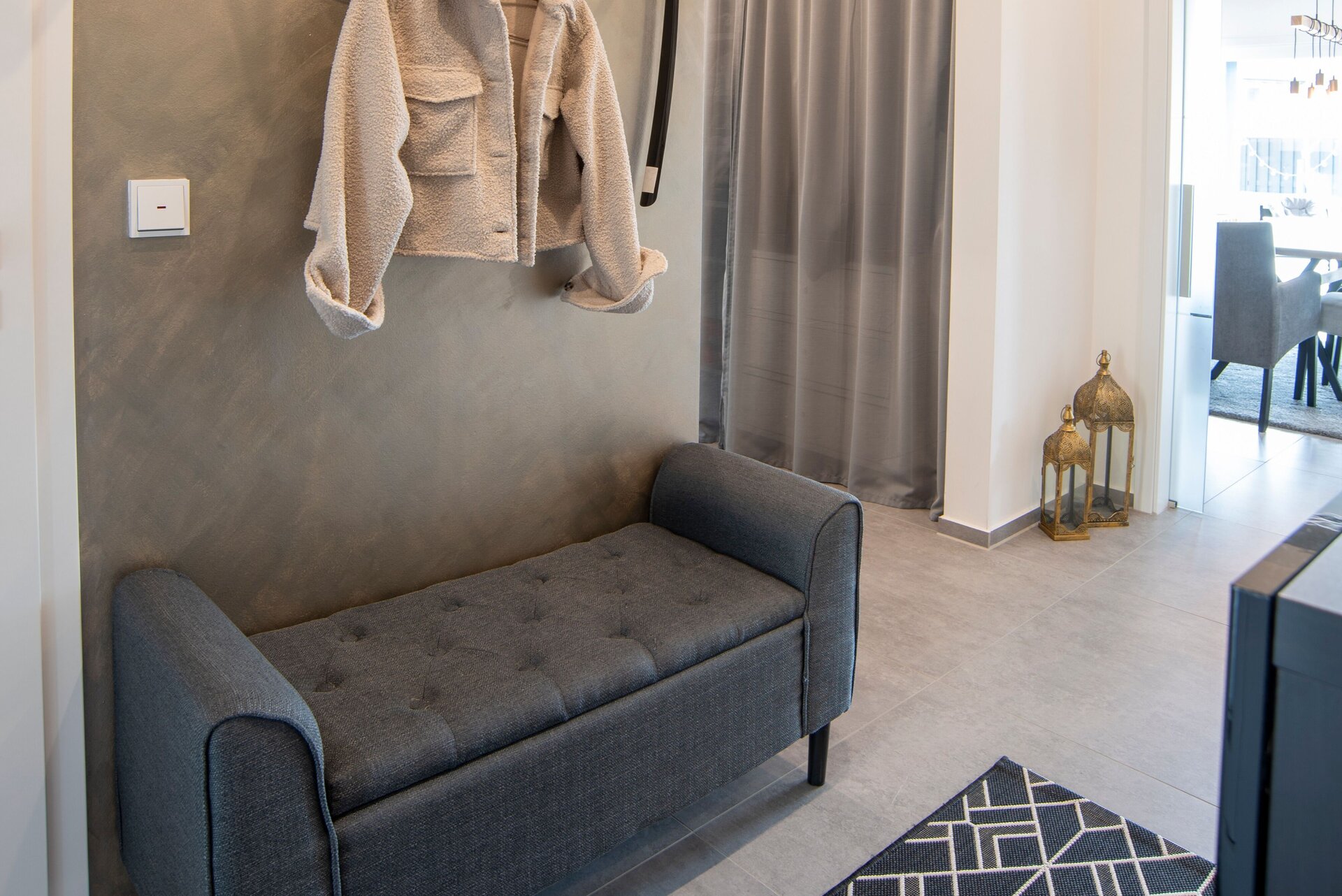 Moderner Eingangsbereich in einem FingerHaus NIVO 130 mit grauer Sitzbank, Garderobe, dekorativen Pflanzen, Wandhaken und Vorhang.