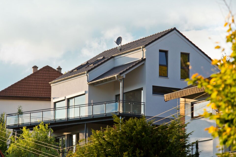 Modernes Einfamilienhaus von FingerHaus in Hanglage mit heller Fassade, großem Balkon mit Glasgeländer und dunklem Satteldach.
