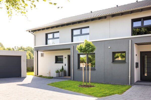 Moderner FingerHaus DUO mit klarer Fassadengestaltung, überdachtem Hauseingang, angrenzender Garage und kleiner Baum im Vorgarten.