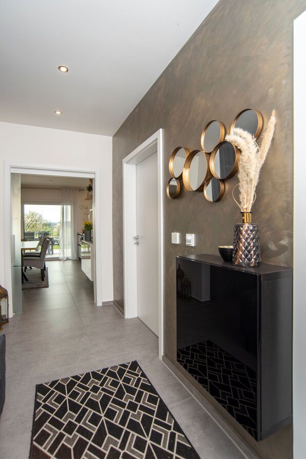 Flur mit grauem Boden, schwarzem geometrischem Teppich, schwarzem Wandregal und dekorativer Vase mit Pampasgras vor grauer Wand mit runden Spiegeln