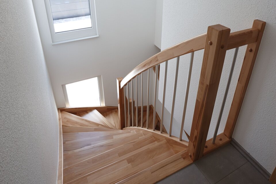 Schmale Treppe mit Holzstufen und Fenster im Treppenhaus.