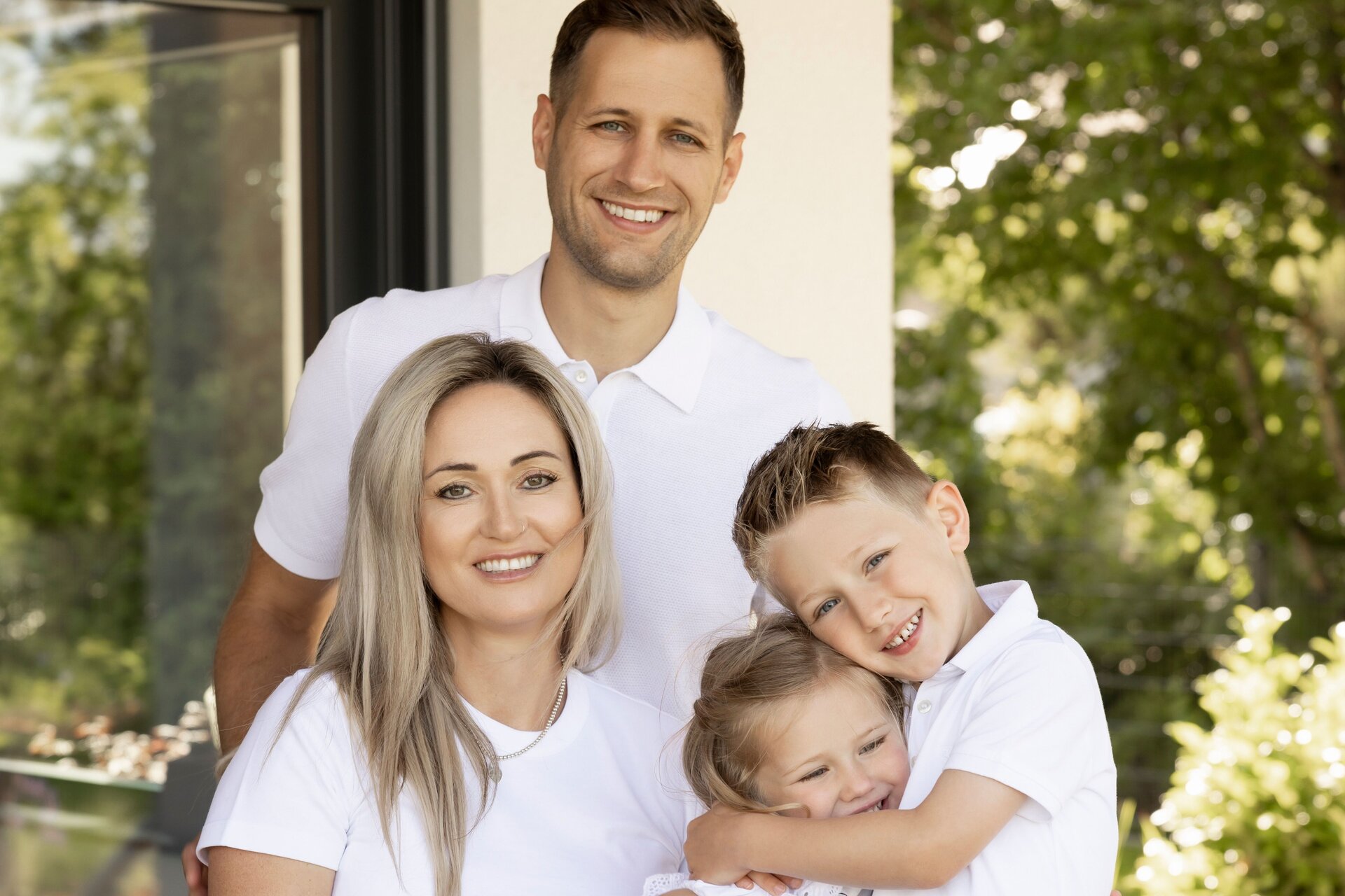 Glückliche Familie in weißer Kleidung sitzt und steht gemeinsam auf der Terrasse eines modernen FingerHaus.